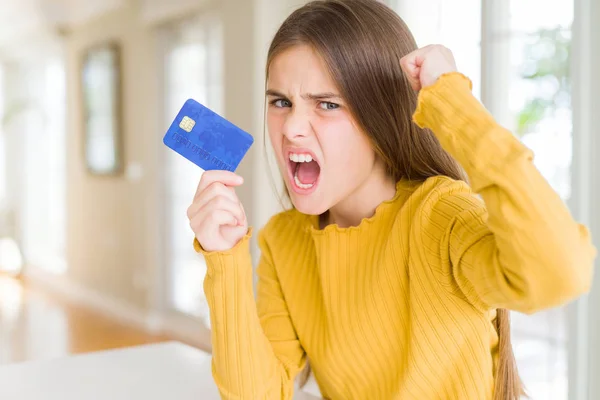 Beautiful young girl kid holding credit card annoyed and frustrated shouting with anger, crazy and yelling with raised hand, anger concept