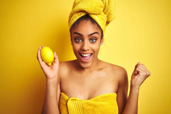 孤立した黄色の背景の上にレモンを保持シャワー後にタオルを身に着けているアフリカ系アメリカ人の女性は誇りと勝利と成功を祝って叫んで非常に興奮し 応援感情 — ストック写真