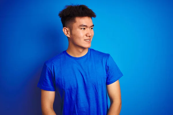 若いアジア系中国人の男性のTシャツを着て隔離された青の背景の上に立って離れて顔に笑みを浮かべて側に見て 自然な表現 自信を持って — ストック写真