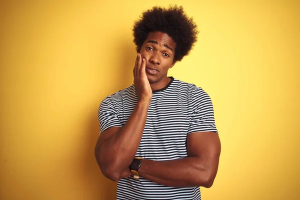 African american man with afro hair wearing navy striped t-shirt over isolated yellow background thinking looking tired and bored with depression problems with crossed arms.