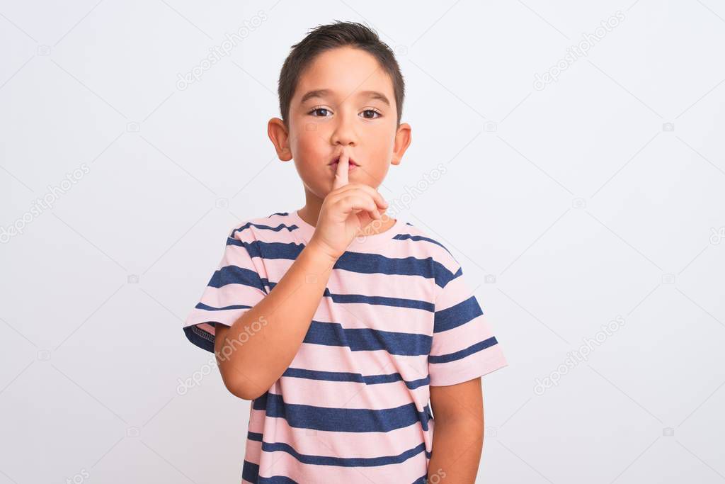 Beautiful kid boy wearing casual striped t-shirt standing over isolated white background asking to be quiet with finger on lips. Silence and secret concept.