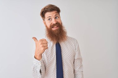 Genç kızıl saçlı İrlandalı işadamı, izole edilmiş beyaz arka planda gülümseyen, gülümseyen ve başparmağıyla yan tarafı gösteren..