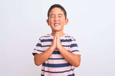 Güzel çocuk, izole edilmiş beyaz arka plan üzerinde sıradan çizgili tişört giyiyor. Yüzünde umut ifadesi olan ve endişeli bir şekilde el ele yalvarıyor ve dua ediyor. Af diliyor. Din kavramı.