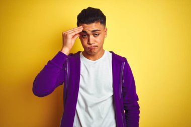 Mor kazak giyen genç Brezilyalı adam izole edilmiş sarı arka planda duruyor. Alnındaki sorun yüzünden endişeli ve stresli. Kriz konusunda endişeli.