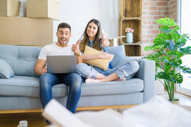Genç ve güzel bir çift yeni evin kanepesinde oturup rahatlıyor. Bilgisayar laptopu kullanıyor. Kocaman gülümsüyor.