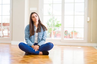 Yüzünde ciddi bir ifadeyle evde yerde oturan güzel bir genç kadın. Basit ve doğal bir şekilde kameraya bakıyorsun..