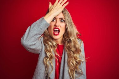 Kırmızı izole edilmiş arka plan üzerinde duran zarif ceketli genç ve güzel bir iş kadını. Yanlışlıkla el ele tutuşarak şaşırmış. Hatayı hatırla. Unuttum, kötü hafıza konsepti.