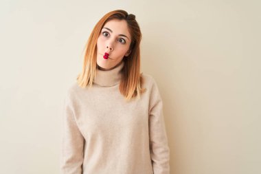 Kırmızı saçlı kadın, zarif balıkçı yaka kazak giyip izole edilmiş beyaz arka planda duruyor. Dudaklı balık suratı yapıyor, çılgınca ve komik bir jest. Komik ifade.