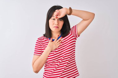 İzole edilmiş beyaz arka plan üzerine kırmızı çizgili tişört giyen genç, güzel Çinli bir kadın. Hastalık, ateş ve soğuk algınlığı için alnına dokunuyor.