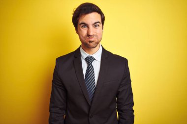 Takım elbiseli ve kravatlı genç yakışıklı işadamı, izole edilmiş sarı arka plan şişirme yanaklarının üzerinde komik bir suratla duruyor. Havayla şişmiş ağız, çılgın bir ifade..