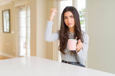 Bir fincan kahve içen genç bir kadın sinirlenmiş ve sinirlenmiş öfkeyle bağırıyor, çıldırmış ve el kaldırarak bağırıyor, öfke konsepti
