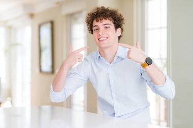 Kıvırcık saçlı genç iş adamı neşeli bir şekilde gülümseyerek parmaklarını ve ağzını gösterdi. Diş sağlığı konsepti.