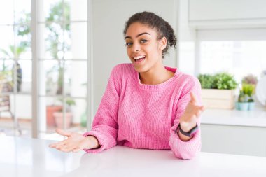 Afro saçlı güzel bir Afro-Amerikan kadını. Günlük pembe süveter giyiyor. Neşeli gülümsüyor, kollarını açıyor.