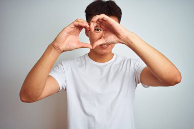 Asyalı genç bir Çinli tişört giyiyor. İzole edilmiş beyaz arka plan üzerinde duruyor. El ve parmakları ile kalp şeklinde.