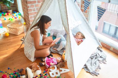 Anaokulunda Tip 'in içinde yerde yatan sarışın kıza güzel bir öğretmen kitabı okuyor.