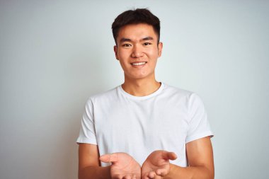 Asyalı genç bir Çinli tişört giyiyordu. İzole edilmiş beyaz arka planda duruyordu. Elleri avuçlarında gülümsüyordu. Tutun ve koruyun