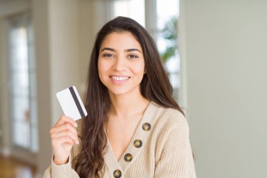 Kredi kartıyla ödeme yapan genç bir kadın mutlu bir yüzle ayakta duruyor ve gülümsüyor dişlerini gösteren bir gülümsemeyle.