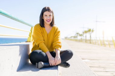 Güzel genç kadın deniz tarafından bir gezinti üzerinde oturan gülümseyen 