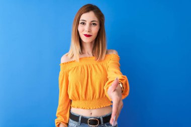 Güzel kızıl saçlı kadın, turuncu günlük tişört giyip mavi arka planda dikiliyor. Dostça bir selamlama ve hoş geldin hediyesi olarak gülümsüyor. Başarılı bir iş..