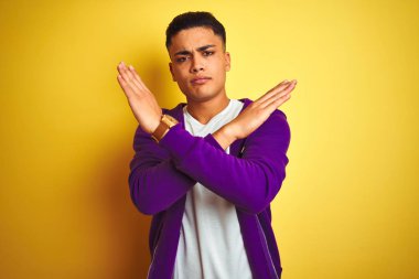 Mor kazak giyen genç Brezilyalı adam izole edilmiş sarı arka planda duruyor. Reddedilmiş yüz ifadesi kollarını kavuşturarak negatif işaret veriyor, kızgın yüz ifadesi takınıyor.