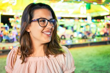 Gözlük takan genç ve güzel bir kadın gecenin ışıklarında mutlu ve heyecanlı bir şekilde gülümsüyor.