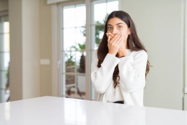 Beyaz masada evde genç güzel kadın hata elleri ile ağız kapsayan şok. Gizli konsept.