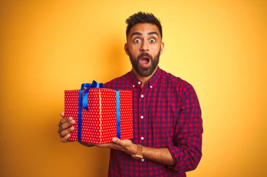 Arap Hintli İspanyol adamın elinde doğum günü hediyesi, izole edilmiş sarı arka planda duruyor. Şaşırmış bir yüzle korkmuş ve korku ifadesinden heyecanlanmış.