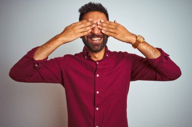 Kırmızı şık gömlek giyen genç Hintli adam izole edilmiş gri arka planda duruyor. Gözleri neşeli ve komik bir şekilde gülümsüyor. Kör kavram.