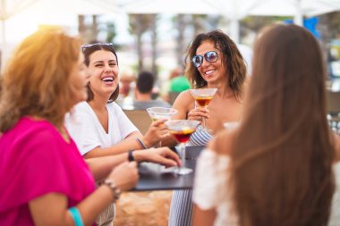 Güzel bir grup kadın restoranın terasında oturmuş kokteyller içiyor konuşuyor ve gülümsüyor.