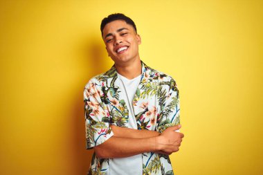 Tatilde olan genç Brezilyalı bir adam izole edilmiş sarı arka plan üzerinde çiçekli gömlek giyiyor ve kollarını kavuşturup kameraya bakıyor. Pozitif kişi.