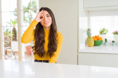 Genç güzel kadın evde el gülümseyen iyi jest yapıyor beyaz masaya göz parmakları ile mutlu yüz üzerinden seyir.