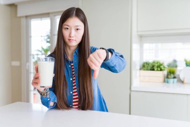 Güzel Asyalı kadın kızgın suratlı bir bardak süt içiyor, negatif işaret baş parmakları aşağıda, reddedilme konsepti.