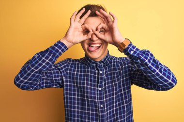 Sarı arka plan üzerinde duran sıradan tişörtlü genç yakışıklı bir adam. Dürbün gibi güzel hareketler yapıyor, gözleri parmaklarından bakıyor. Çılgın ifade.