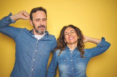 Güzel orta yaşlı çift, izole edilmiş sarı arka planda dikiliyorlar. Yorgun, rahat, uykulu ve sabahın erken saatlerinde esniyorlar.