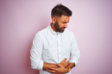 Genç Hintli iş adamı zarif bir gömlek giyer ve midesi bulanan, acı verici bir hastalıktan dolayı el üstünde pembe arka planda dikilir. Ache kavramı.