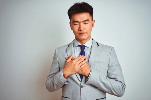 灰色のジャケットを着たアジア系中国人ビジネスマンが 目を閉じて胸の上で手を笑顔で孤立した白い背景の上に立ってネクタイをし 顔に感謝のジェスチャー 健康コンセプト — ストック写真