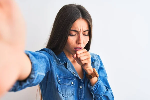 Beautiful woman wearing denim shirt make selfie by camera over isolated white background feeling unwell and coughing as symptom for cold or bronchitis. Healthcare concept.