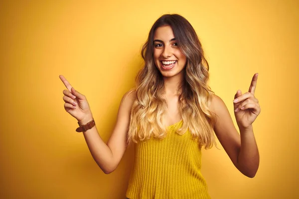 黄色の隔離された背景の上にTシャツを着て若い美しい女性は 異なる方向に指で自信を持って指して笑顔 広告のコピースペース — ストック写真