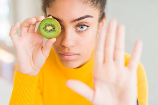 若いですアフリカ系アメリカ人の女の子食べる緑色Kiwiとともにオープン手Doing停止サインとともに深刻なと自信を持って式 防衛ジェスチャー — ストック写真