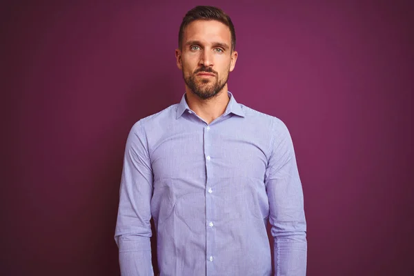 Young business man wearing elegant shirt over purple isolated background with serious expression on face. Simple and natural looking at the camera.