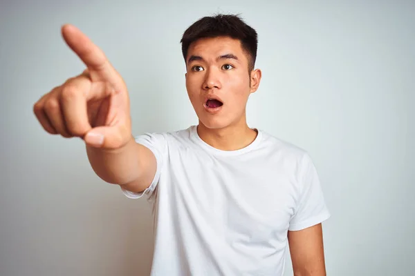 年轻的亚裔男子穿着T恤衫站在孤立的白色背景上 带着惊讶的手指指尖着前方 张开嘴惊讶的表情 前面有什么东西 — 图库照片