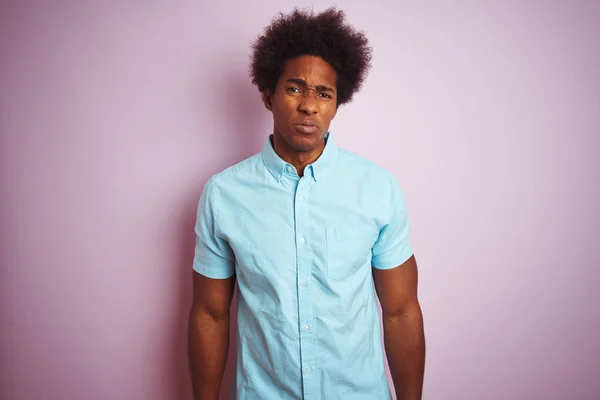 Young american man with afro hair wearing blue shirt standing over isolated pink background depressed and worry for distress, crying angry and afraid. Sad expression.