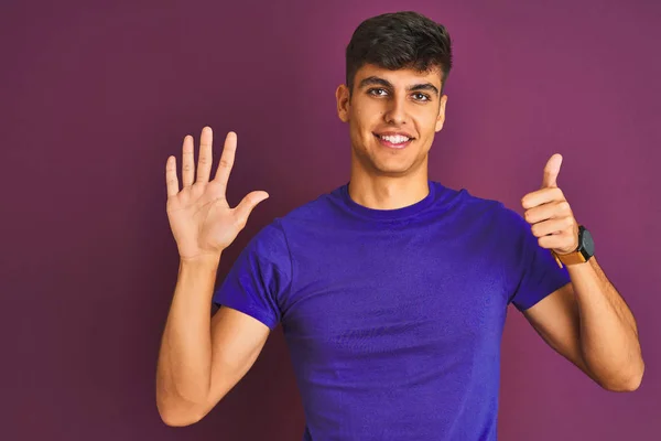 自信と幸せ笑顔ながら 指の番号6で表示され 指差す紫色の背景に立ってTシャツを着て若いインド人男性 — ストック写真