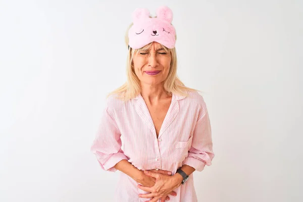 Middle age woman wearing sleep mask and pajama over isolated white background with hand on stomach because indigestion, painful illness feeling unwell. Ache concept.