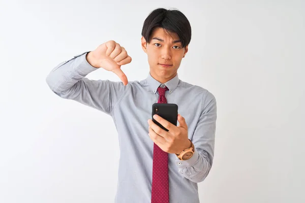 中国商人打着领带 用智能手机站在孤独的白色背景上 满脸怒容 负面迹象表明不喜欢戴大拇指 拒绝的概念 — 图库照片