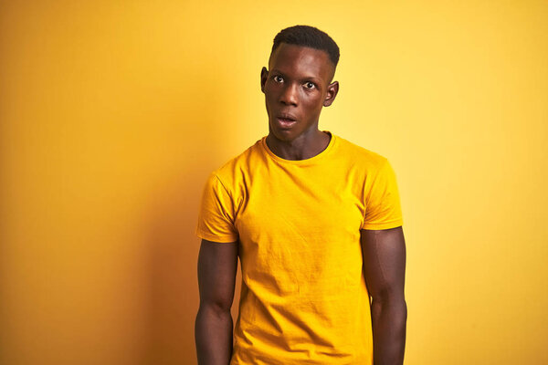 Young african american man wearing casual t-shirt standing over isolated yellow background In shock face, looking skeptical and sarcastic, surprised with open mouth