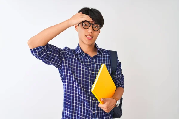 Chinese student man wearing backpack holding notebook over isolated white background stressed with hand on head, shocked with shame and surprise face, angry and frustrated. Fear and upset for mistake.