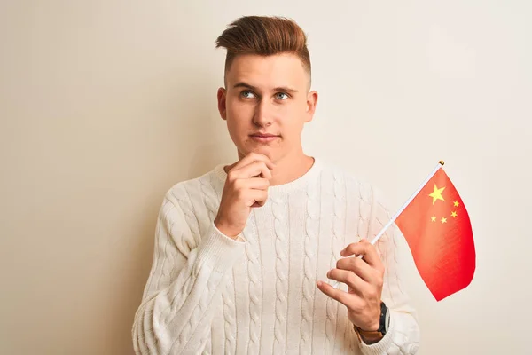 Young handsome man holding Chinese China flag over isolated white background serious face thinking about question, very confused idea