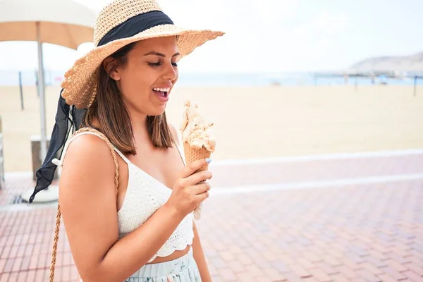 Young beautiful woman eating ice cream cone by the beach on a sunny day of summer on holidays