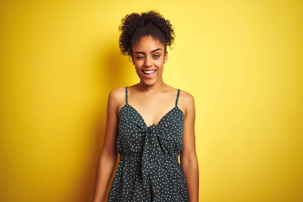 African american woman wearing summer casual green dress over isolated yellow background winking looking at the camera with sexy expression, cheerful and happy face. — Stock Image African American Woman Wearing Summer Casual Green Dress Isolated Yellow Royalty Free Stock Photos